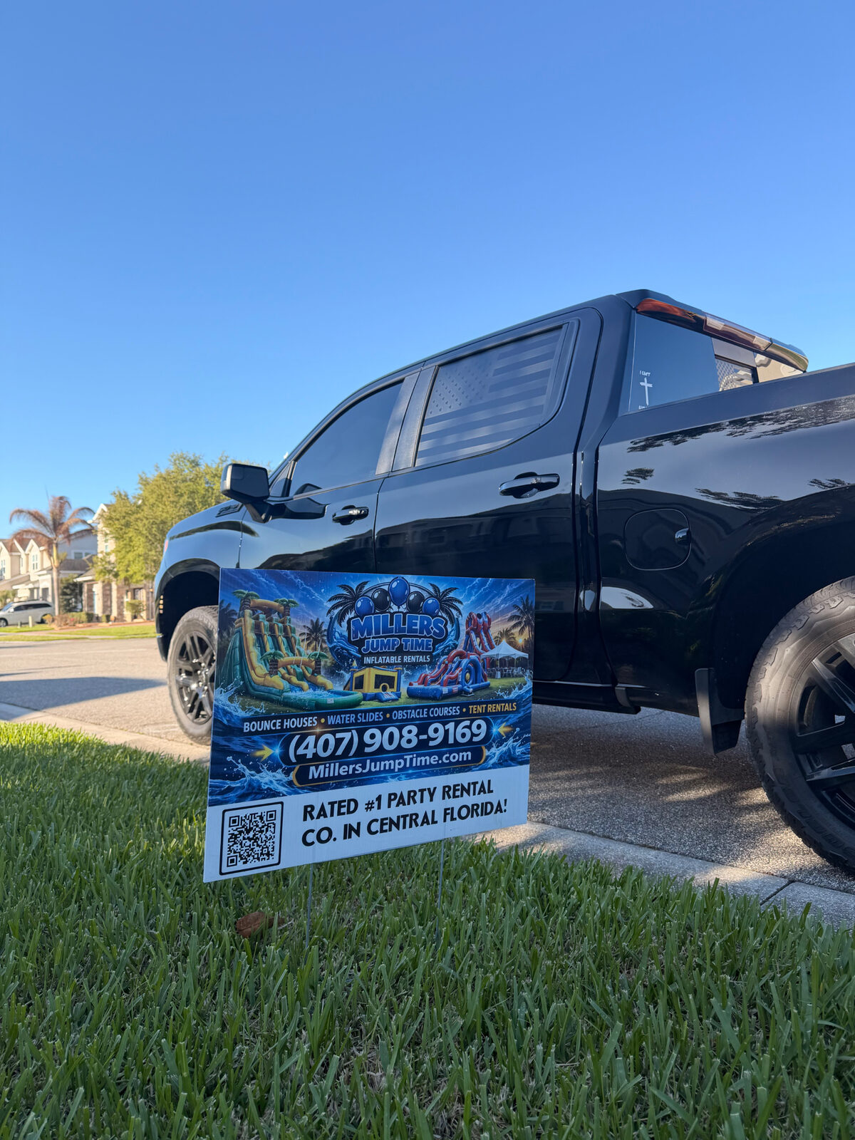 Branded yard sign with QR code staked at the curb of a customer's home next to a Miller's Jump Time Entertainment truck.